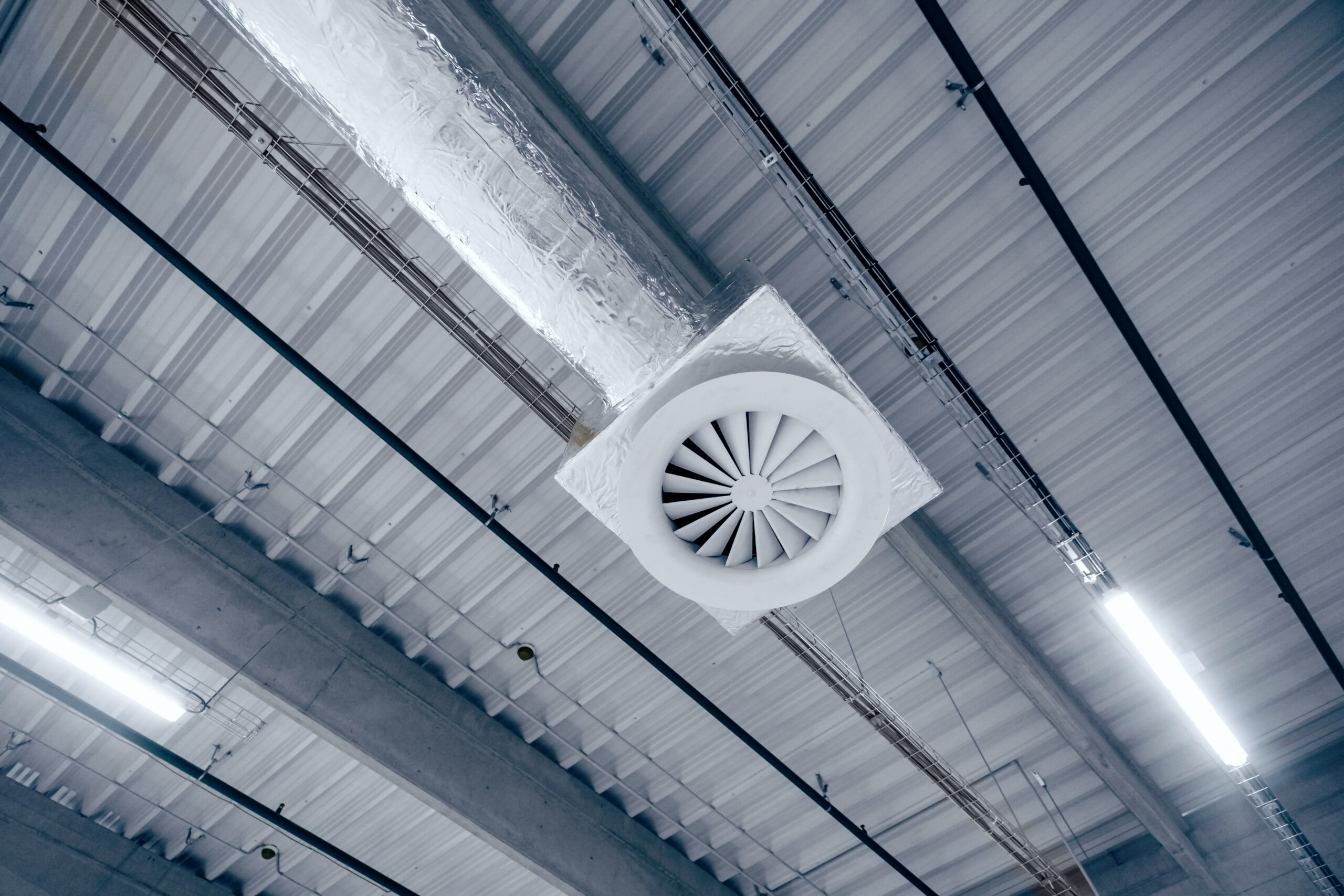 Air ventilation system on the ceiling in a large warehouse. Pipes made of silver insulating material hang from the ceiling inside the new building